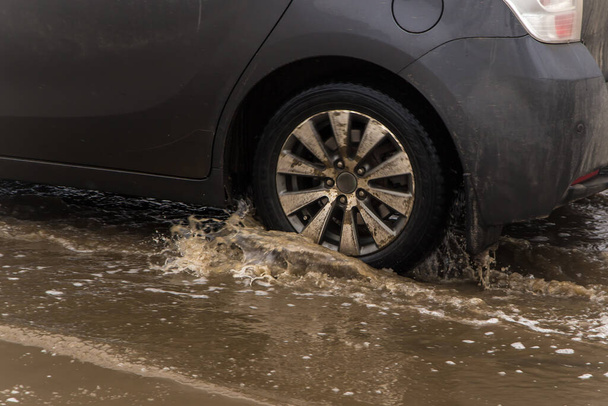 The wheel of a car driving through a deep muddy puddle of melted snow. - 写真・画像