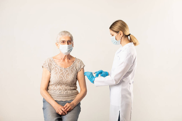A doctor giving an injection of a covid-19 vaccine to an elderly patient. Vaccination concept. - Photo, image