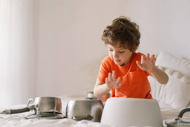 Roztomilý mladý chlapec používající dřevěné tyčinky na bouchání talířů, které jsou nastaveny jako bubny. Doba karantény - Fotografie, Obrázek