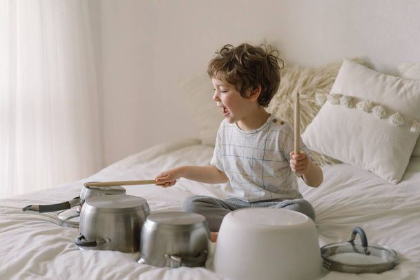 Roztomilý mladý chlapec používající dřevěné tyčinky na bouchání talířů, které jsou nastaveny jako bubny. Doba karantény - Fotografie, Obrázek