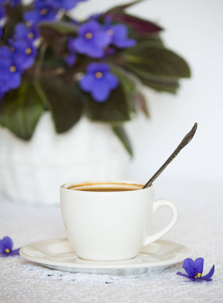 una taza de café negro sobre la mesa con una flor violeta casera. - Foto, imagen