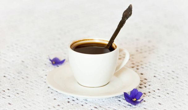 filiżanka kawy i spodek z fioletowymi kwiatami afrykańskiego fioletu na białym tle stołu. - Zdjęcie, obraz