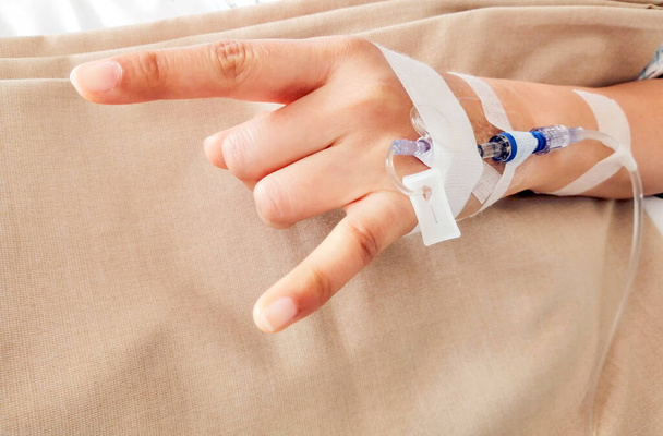 Pacjentka, która zrobiła znak miłosny, siedzi na łóżku w szpitalu z roztworem soli fizjologicznej pod ręką.. - Zdjęcie, obraz