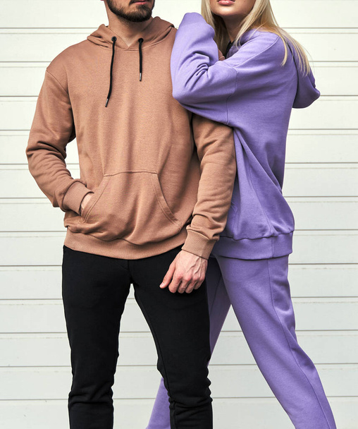 couple en tenue de rue décontractée. Homme debout dans un pull en daim brun. Femme porte rose violet polaire sweat à capuche et pantalon - Photo, image