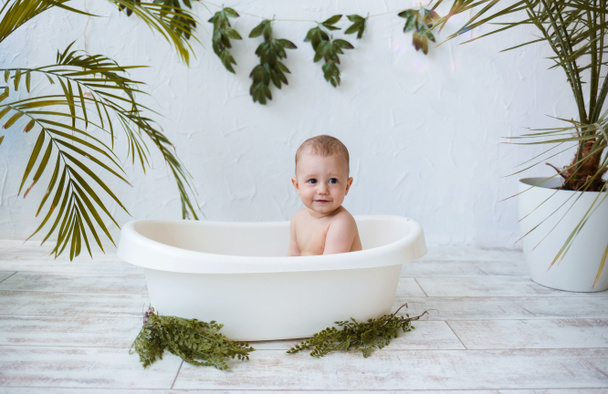 egy kisfiú fürdik egy fehér fürdőben, növényekkel, fehér háttérrel, szöveges szöveggel. Vízkezelés gyermekek számára nyáron - Fotó, kép