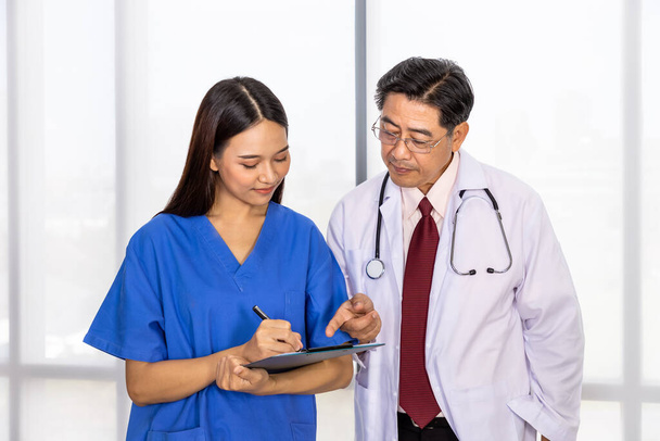 Happy Asian male and female medical doctor standing and discussing about case with notepad - Photo, Image