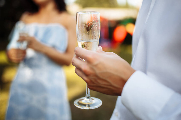 Muž se sklenicí šampaňského v rukou na pozadí společnosti oslavující lidi. Svatba, narozeniny, výročí. Skupina lidí si užívá šampaňského na svatební hostině - Fotografie, Obrázek