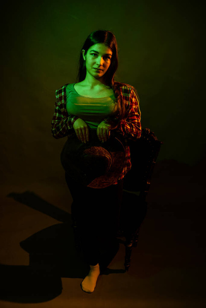A girl in a plaid shirt with a cowboy hat illuminated by multicolored light - Photo, image
