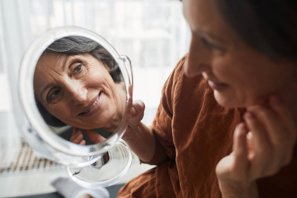 Mature woman looking at the mirror at the results of the makeup - Valokuva, kuva