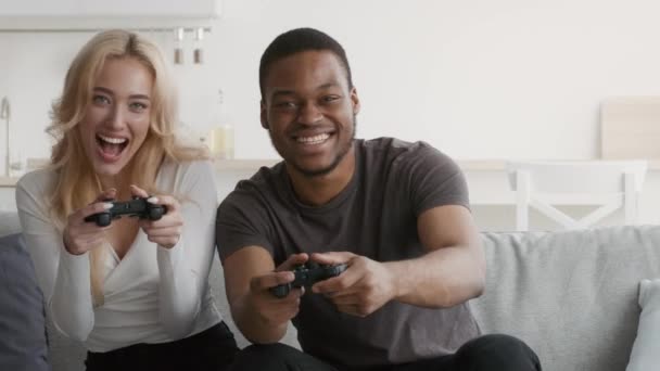 Pareja multiétnica jugando videojuegos sentada en un sofá en casa - Imágenes, Vídeo
