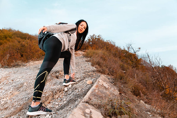 Turystyka i sport rekreacyjny. Koncepcja sukcesu. Młoda kobieta z plecakiem na plecach wspina się na skały. Widok dolny. - Zdjęcie, obraz