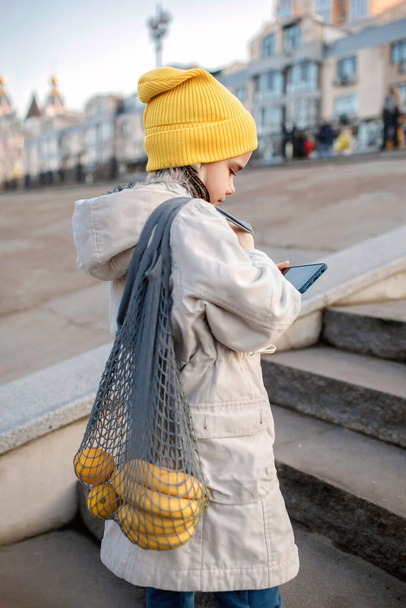 Preteen girl sitting on street stairs and SMS with smartphone on way from shopping - Foto, Bild