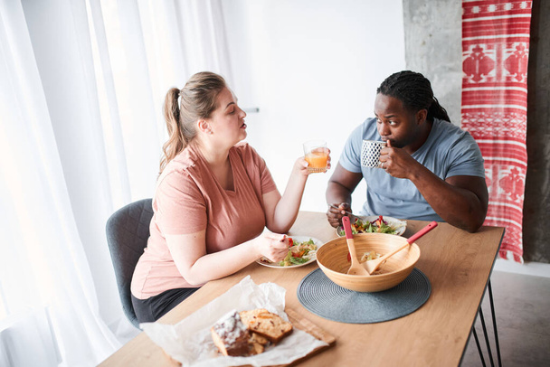 Couple talking during breakfast while sitting at the kitchen and eating salad - Fotó, kép