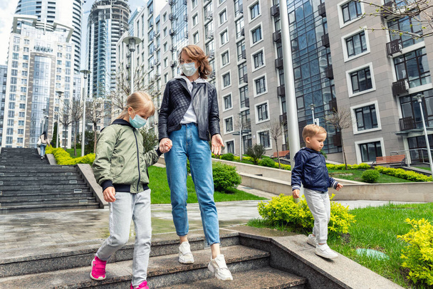 Jeune mère caucasienne adulte marchant en bas avec fils et fille enfants dans le centre-ville contre la construction. Nouveau mode de vie urbain normal après le coronavirus - Photo, image