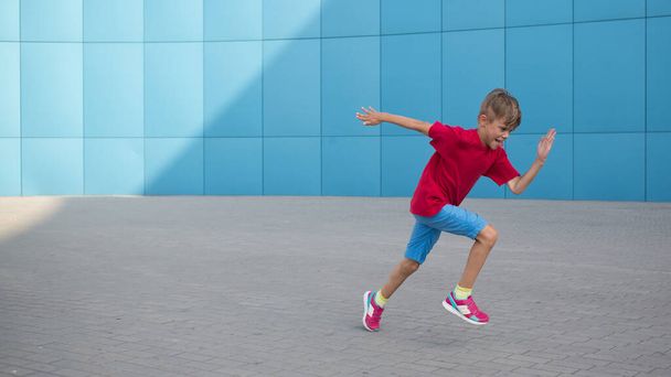 Cute little boy running over blue wall, urban scene - Фото, изображение
