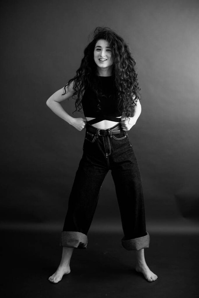 simple and stylish portrait of a curly brunette, free posing for the camera, black soft focus - Foto, imagen