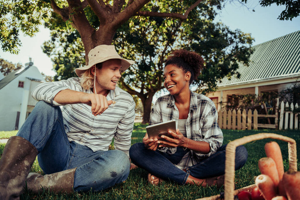 Mixed race couple sitting together chatting about images on digital tablet bonding - Valokuva, kuva