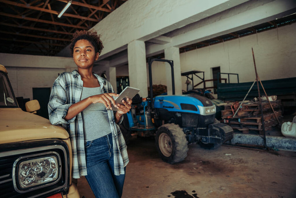 Mixed race female wearing checkered flannel carrying digital tablet in barn - Foto, Bild