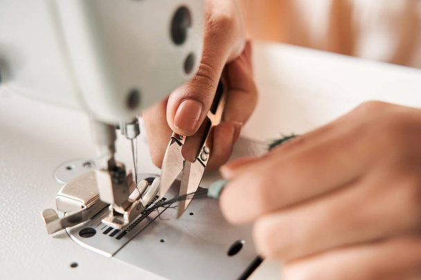 Woman cutting threads with scissors while finished re sewing clothes - Foto, Bild
