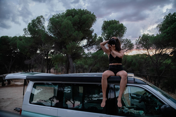 Mujer sentada en el techo de una caravana en el bosque al atardecer - Foto, Imagen
