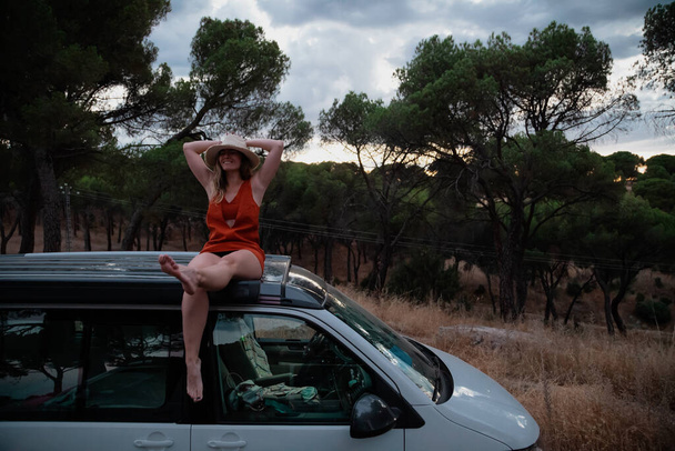 Mujer sentada en el techo de una caravana en el bosque al atardecer - Foto, Imagen