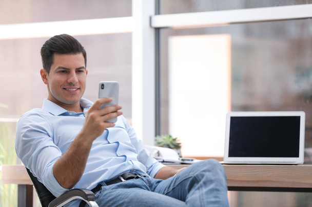 Businessman using smartphone in office chair at workplace - Foto, Bild