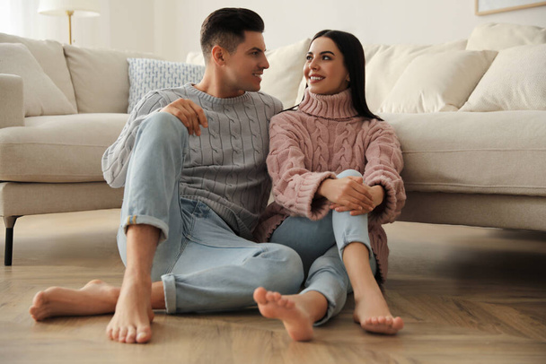 Happy couple sitting on warm floor in living room. Heating system - Foto, Imagem