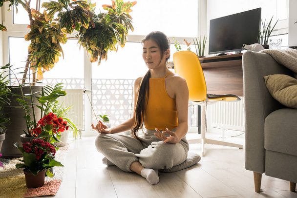Woman in casual clothes meditating and sitting at lotus pose at home - Photo, Image
