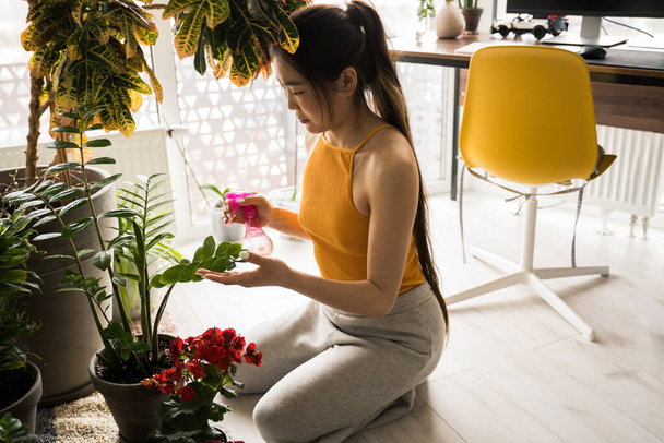 Florist is standing at home and holding a sprinkler while taking care of her flowers - Фото, изображение
