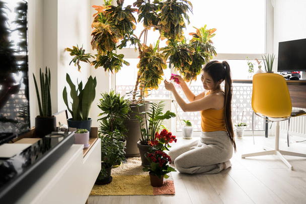 Woman sprays plants in flower pots while sitting at the floor - Valokuva, kuva