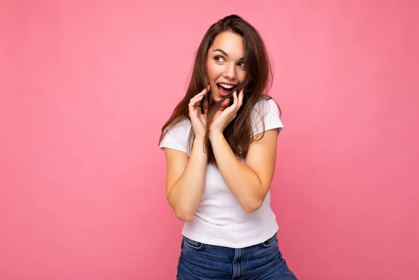 Φωτογραφία πορτρέτο του νεαρού όμορφο χαμογελαστό hipster μελαχρινή γυναίκα σε λευκό t-shirt με mockup. Σέξι ξέγνοιαστη γυναίκα που ποζάρει απομονωμένη κοντά σε ροζ τοίχο με άδειο χώρο στο στούντιο. Θετικό μοντέλο - Φωτογραφία, εικόνα