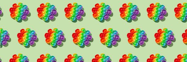 Banner patroon gemaakt met regenboog pop het fidget speelgoed op groene achtergrond. Duw bubbel fidget zintuiglijk speelgoed - wasbaar en herbruikbaar stress-reliëf speelgoed. Antistress speelgoed voor kinderen of volwassenen - Foto, afbeelding