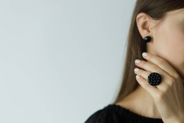 Beautiful stylish woman with modern round black ring and earring, space for text. Fashionable female in black dress with unusual fused glass accessory and manicure. Beauty and care. - Foto, imagen