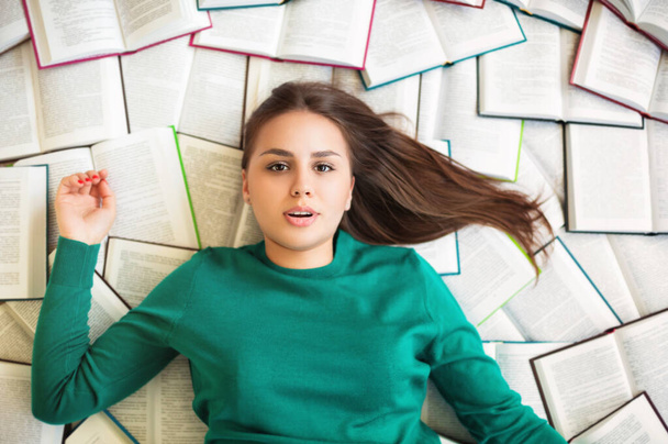 Vista dall'alto della studentessa bruna sdraiata sui libri e che legge durante la preparazione dell'esame - Foto, immagini