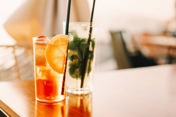 Ângulo alto de copos com coquetéis frios doces e palhas colocadas na mesa no bar no dia de verão - Foto, Imagem