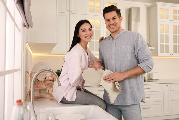 Happy couple with clean dishes in kitchen - Photo, Image