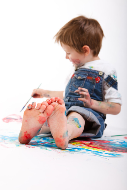 Funny photo of cute 5 years old boy painting on white background. Focus on feet. - Foto, Imagen