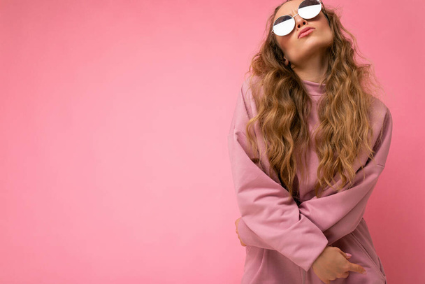 Attractive amusing young blonde woman wearing everyday stylish clothes and modern sunglasses isolated on colorful background wall looking up and having fun - Photo, Image