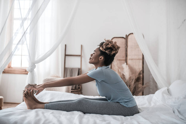 African american woman sitting on bed holding toes - Fotoğraf, Görsel