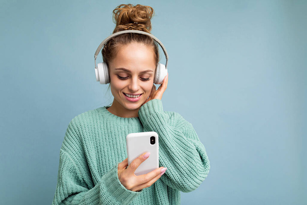 Photo shot of beautiful joyful smiling young female person wearing stylish casual outfit isolated over colorful background wall wearing white bluetooth wireless earphones and listening to music and - Fotografie, Obrázek