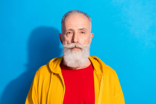 Photo portrait of serious old man wearing hoody isolated on bright blue color background - 写真・画像