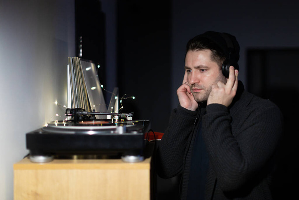 Νεαρός όμορφος άντρας της χιλιετίας ακούει μουσική με ακουστικά στο σκοτεινό μπακάλικο. - Φωτογραφία, εικόνα