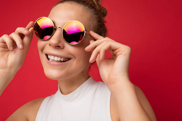 Closeup photo of attractive smiling happy young blonde woman wearing everyday stylish clothes and modern sunglasses isolated on colorful background wall looking at camera - Zdjęcie, obraz
