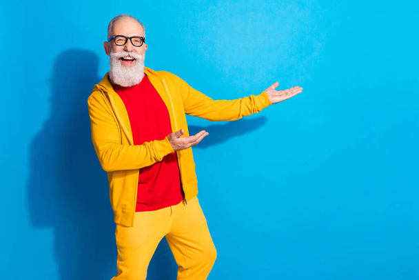 Photo of happy excited funky funny mature man demonstrating product advertisement isolated on blue color background - Fotografie, Obrázek