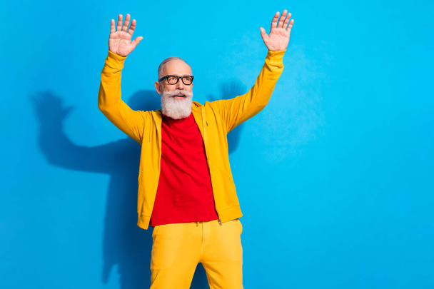Photo of funky funny smiling mature man in glasses dancing having fun wear yellow suit isolated on blue color background - Zdjęcie, obraz