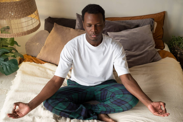 Young african man meditating sitting at his bedroom in the morning - Photo, Image