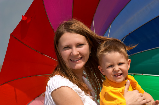 Do not depend on weather conditions. Happy young woman and kid under brightly colored umbrella having fun outdoors. - Foto, imagen