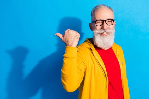 Photo of happy positive handsome cheerful mature man in glasses advertising product isolated on blue color background - Photo, image
