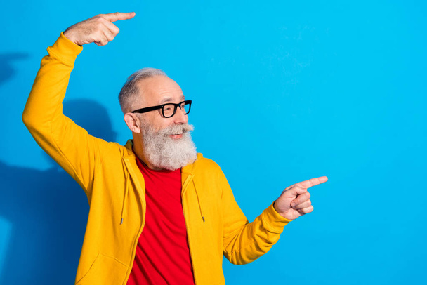 Photo of happy good mood positive mature man in glasses advertising product point finger copyspace isolated on blue color background - Foto, afbeelding