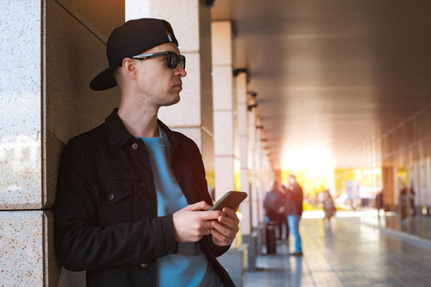moda elegante chico negro gorra gafas de sol con auriculares smartphone fondo urbano atardecer - Foto, imagen